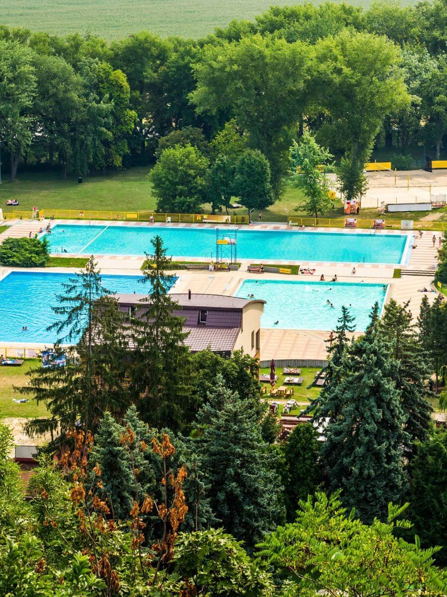 Elevated view of three outdoor swimming pools surrounded by green trees